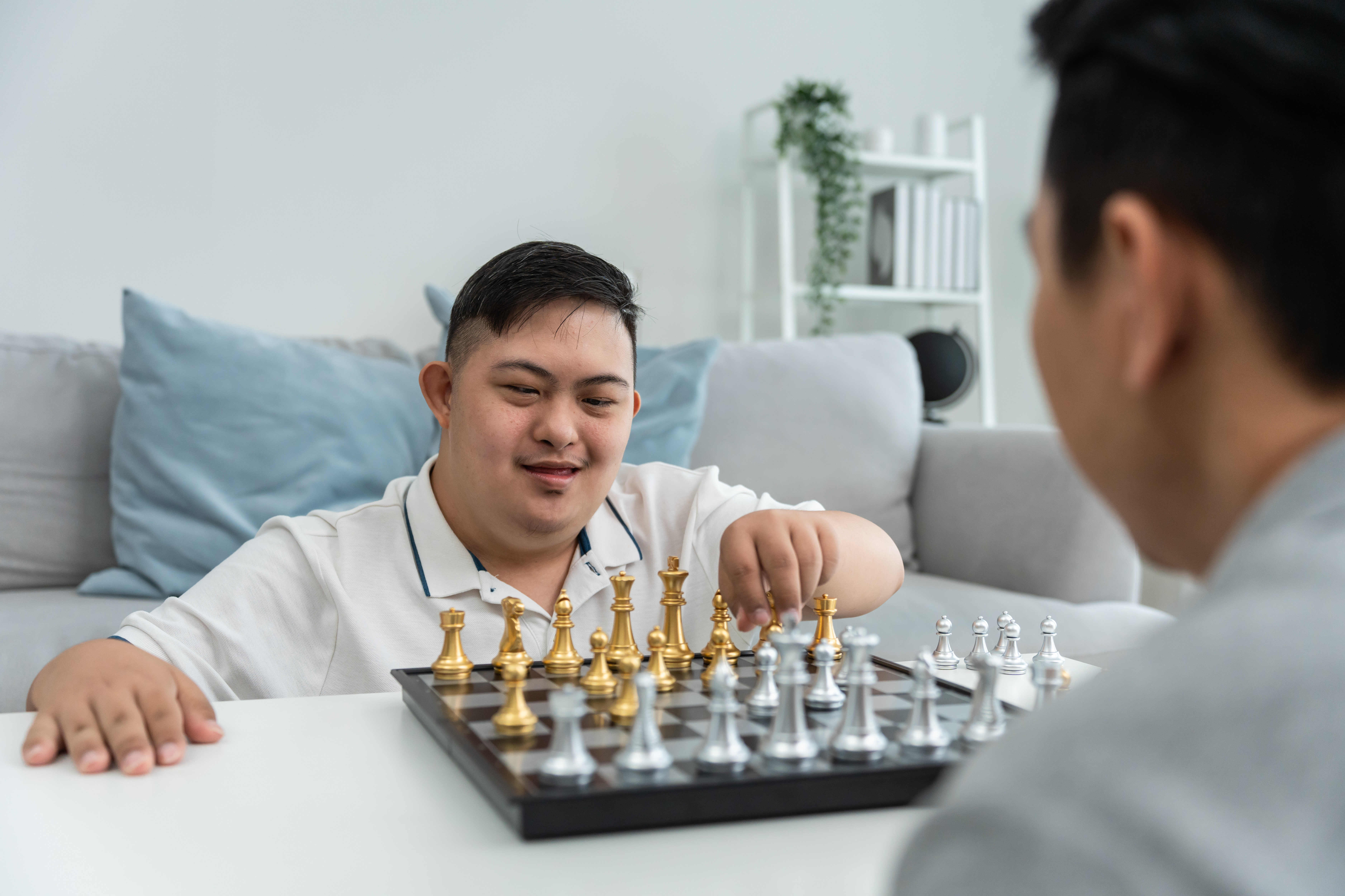 Asian attractive father play chess game with his son in living room.
