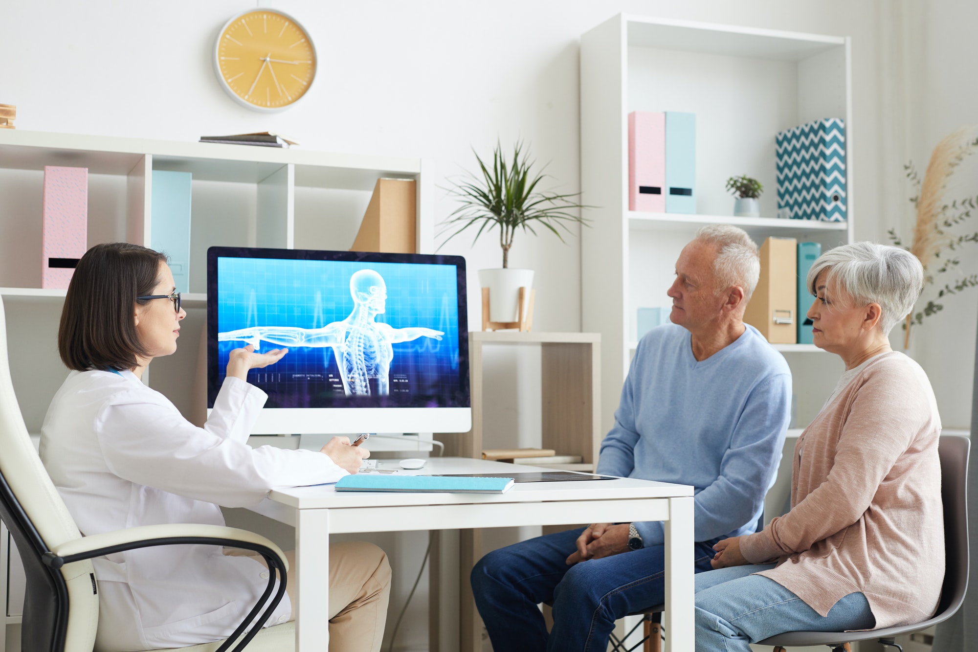 doctor and two elderly people looking at an X-ray image of a torso on a computer